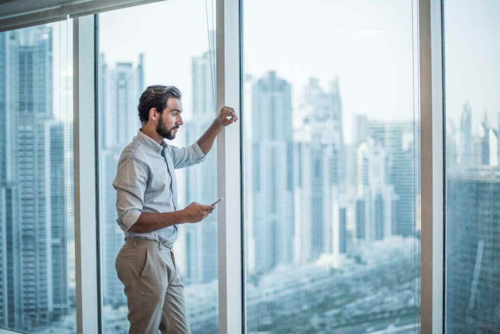 Businessman Arif Patel with smartphone staring through window with skyscraper view, Dubai, United Arab Emirates